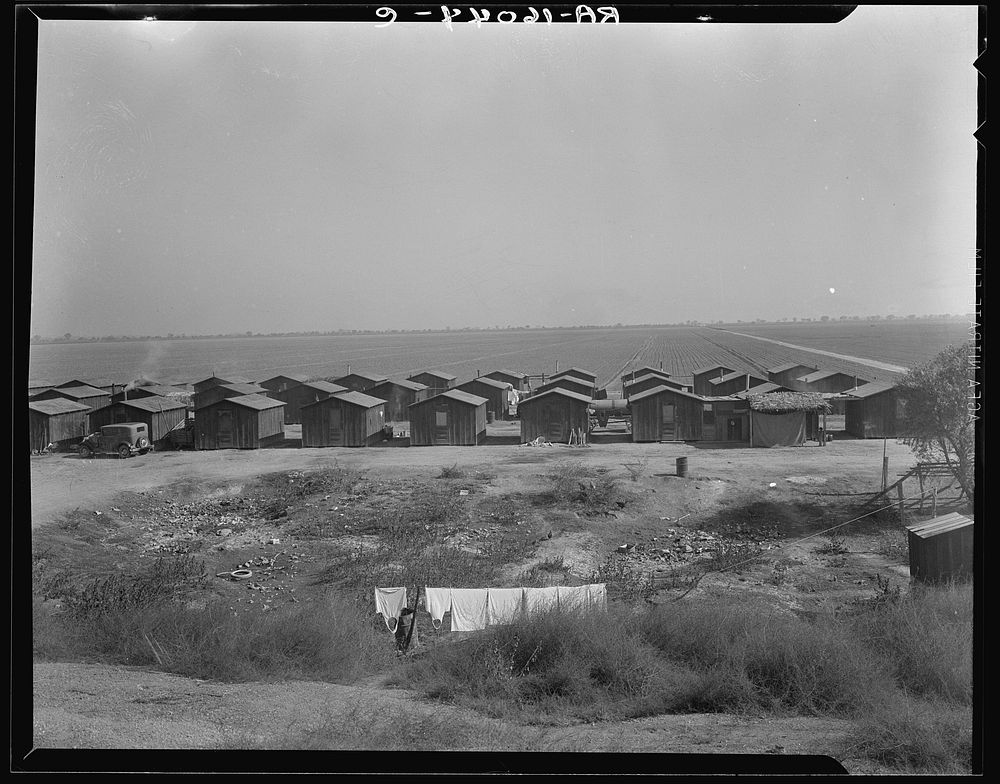 Company housing for Mexican cotton pickers, showing the San Joaquin Valley in the background. South of Corcoran, California.…