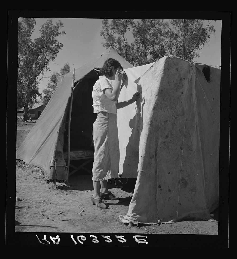 Woman in a California pea pickers' camp, mending the tent. Sourced from the Library of Congress.