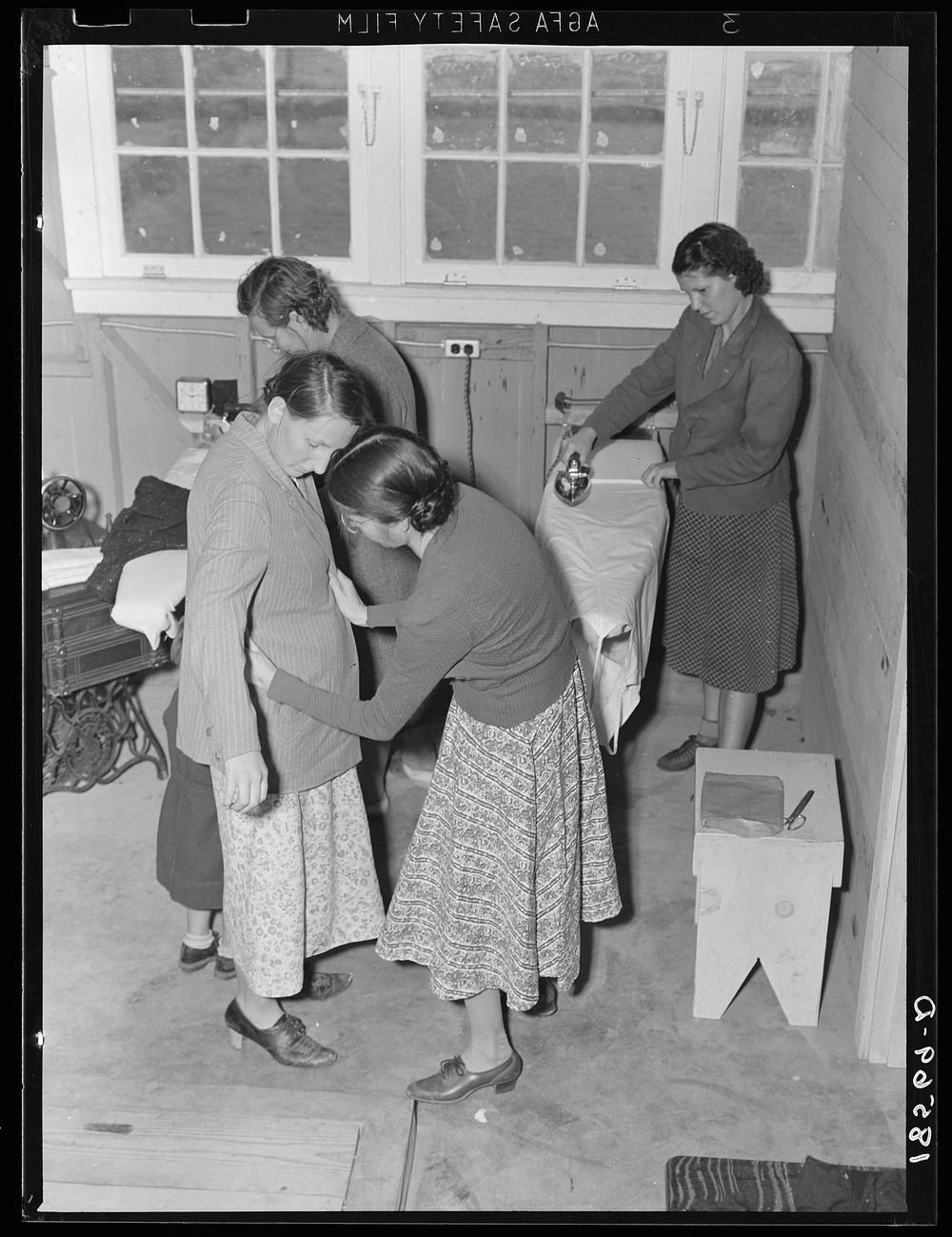Camper receives help in fitting a coat from Works Progress Administration (WPA) sewing instructor. Shafter camp for…