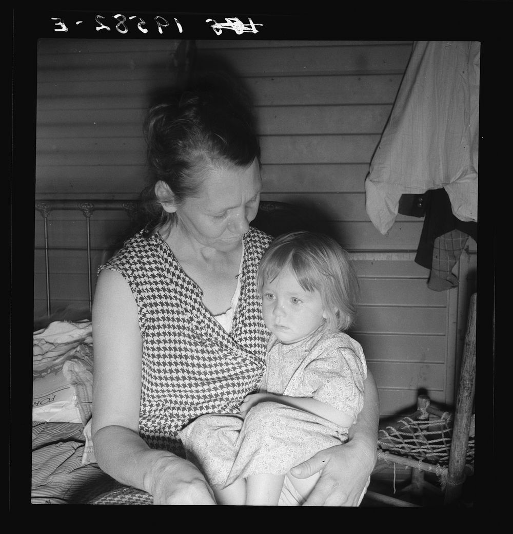 Farm Security Administration (FSA) camp at Farmersville, California. Mother from Oklahoma, migrant, awaits visit of resident…