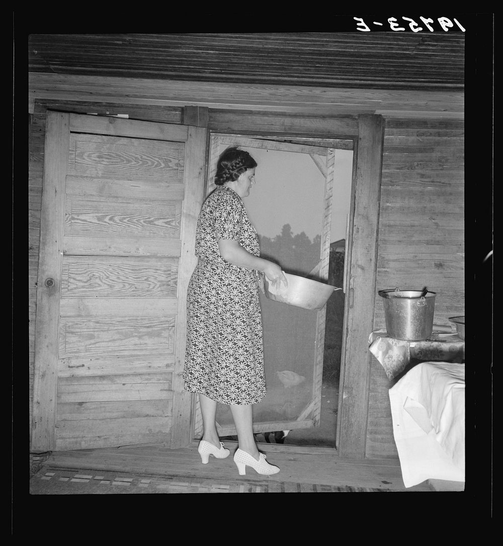 Tobacco sharecropper's wife disposing of dishwater after washing breakfast dishes. She put on white shoes for the…