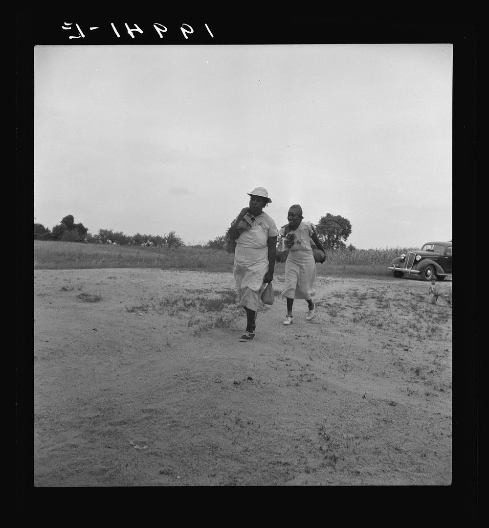 Mother of sharecropper family and friend coming up the road in the rain, bringing home sacks of vegetables from the neighbor…