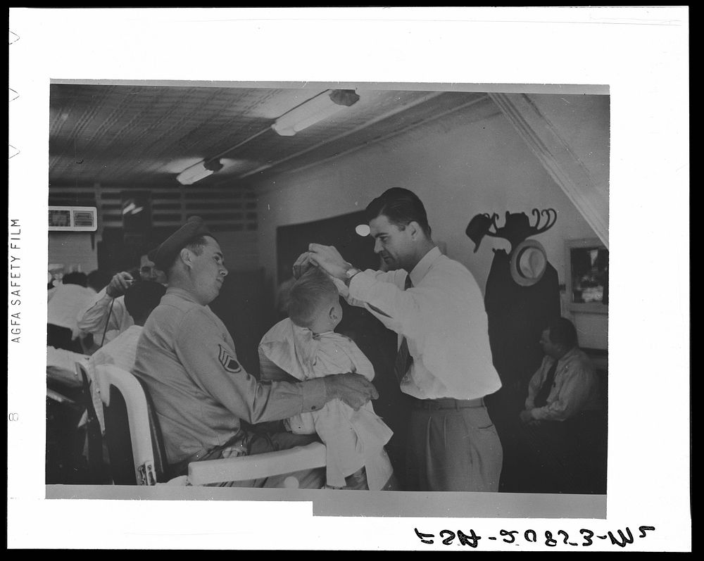 Sergeant from Fort Benning getting his son's hair cut at a barber shop in Columbus, Georgia. Sourced from the Library of…