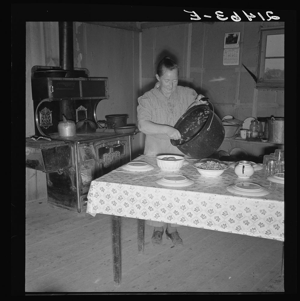 Mrs. Wardlow getting dinner after church in her basement dugout home. Dead Ox Flat, Malheur County, Oregon. Sourced from the…