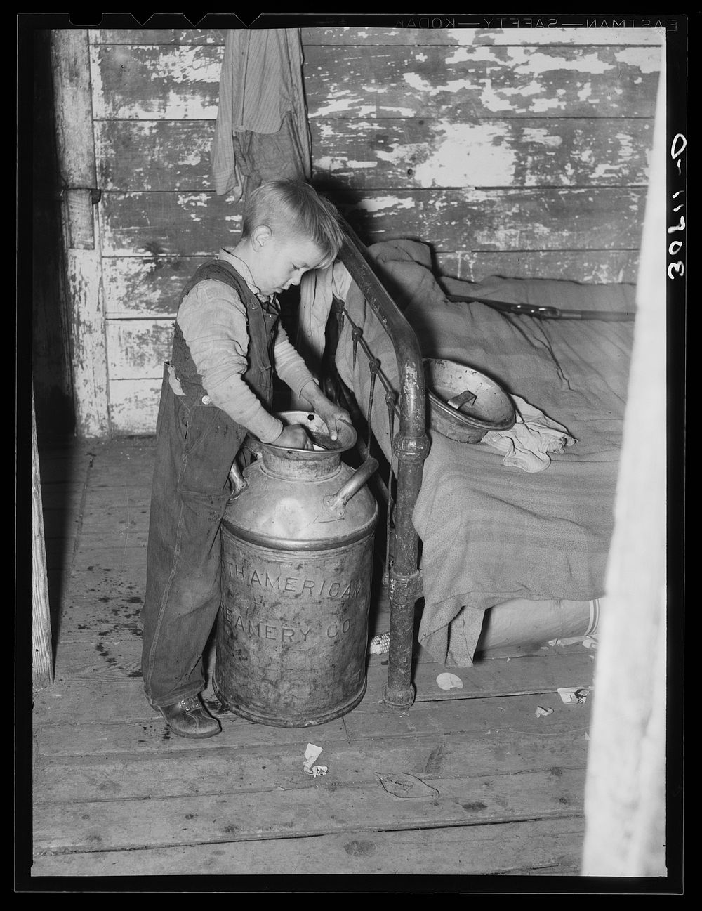 Son of Joe Kramer dipping water from a milk can. Near Williston, North Dakota by Russell Lee