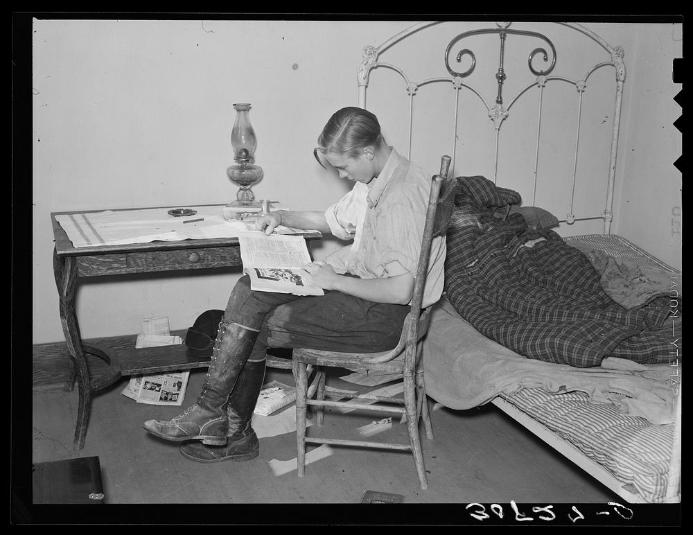 Boy reading in bedroom. Note lack of proper bed clothing. Home of A.O. Ryland near Williston, North Dakota by Russell Lee