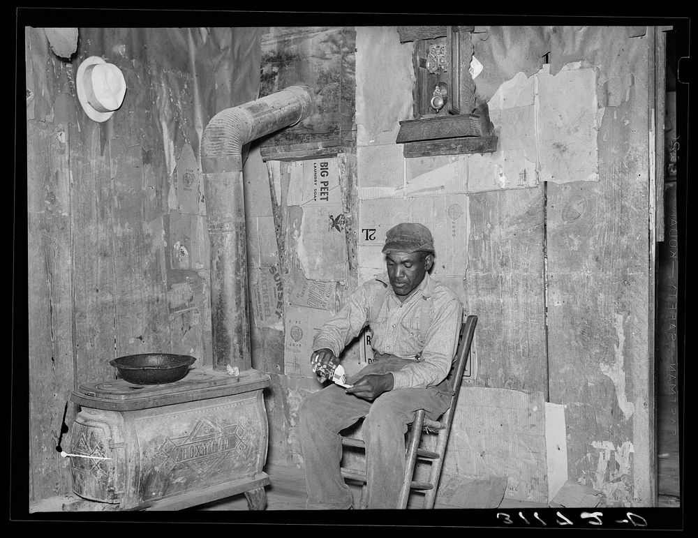 New Madrid County, Missouri. Sharecropper rolling cigarette in living room of shack home by Russell Lee
