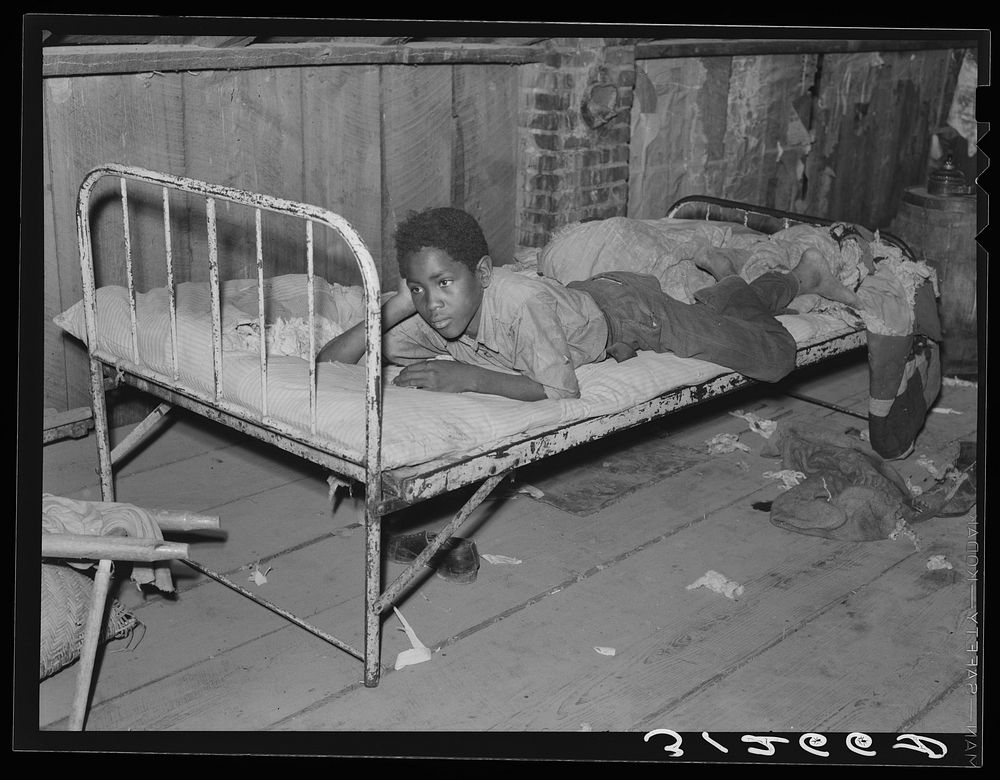 Boy resting on bed in attic of sharecropper shack. New Madrid County, Missouri by Russell Lee