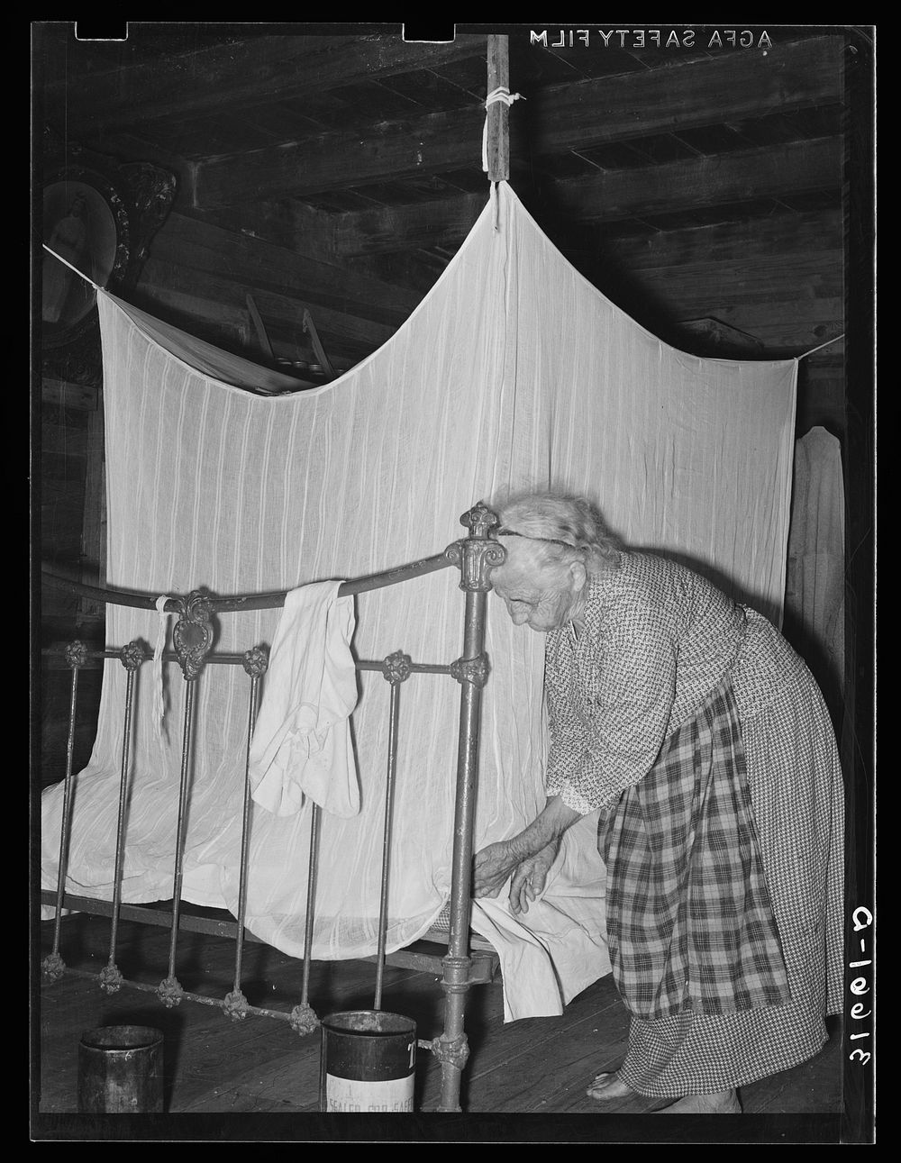 Aged Cajun woman tucking in mosquito bar under mattress. Near Crowley, Louisiana by Russell Lee
