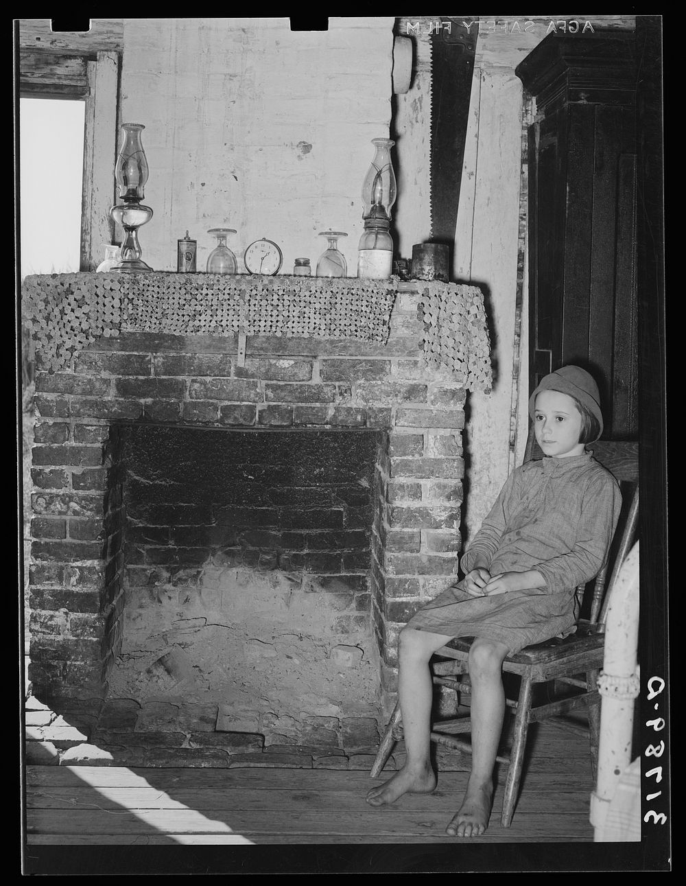 Daughter of Cajun day laborers sitting in front of fireplace in home near New Iberia, Louisiana by Russell Lee