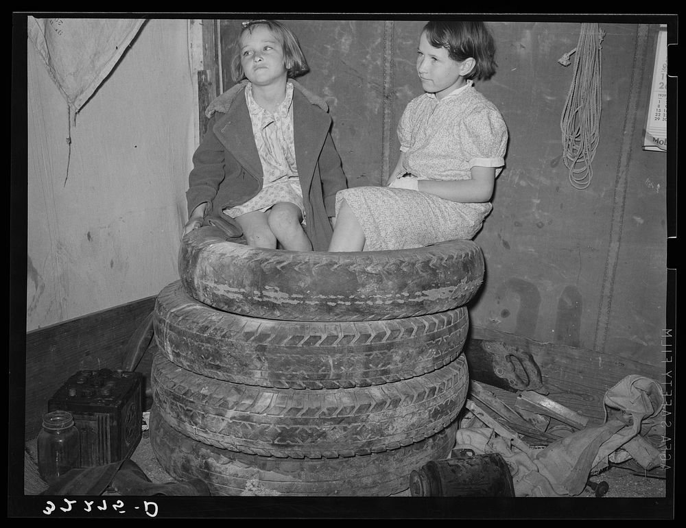 Daughters of  migrant auto wrecker sitting on tires in corner of tent home. Nueces Bay, Corpus Christi, Texas by Russell Lee