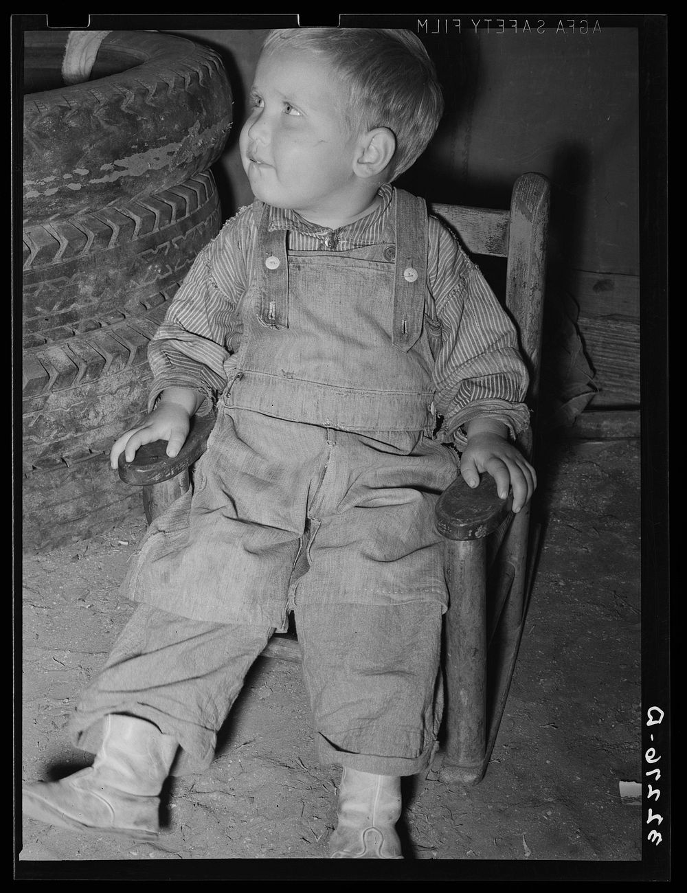 [Untitled photo, possibly related to: Child of  migrant auto wrecker sitting next to tires in corner of tent home. Nueces…