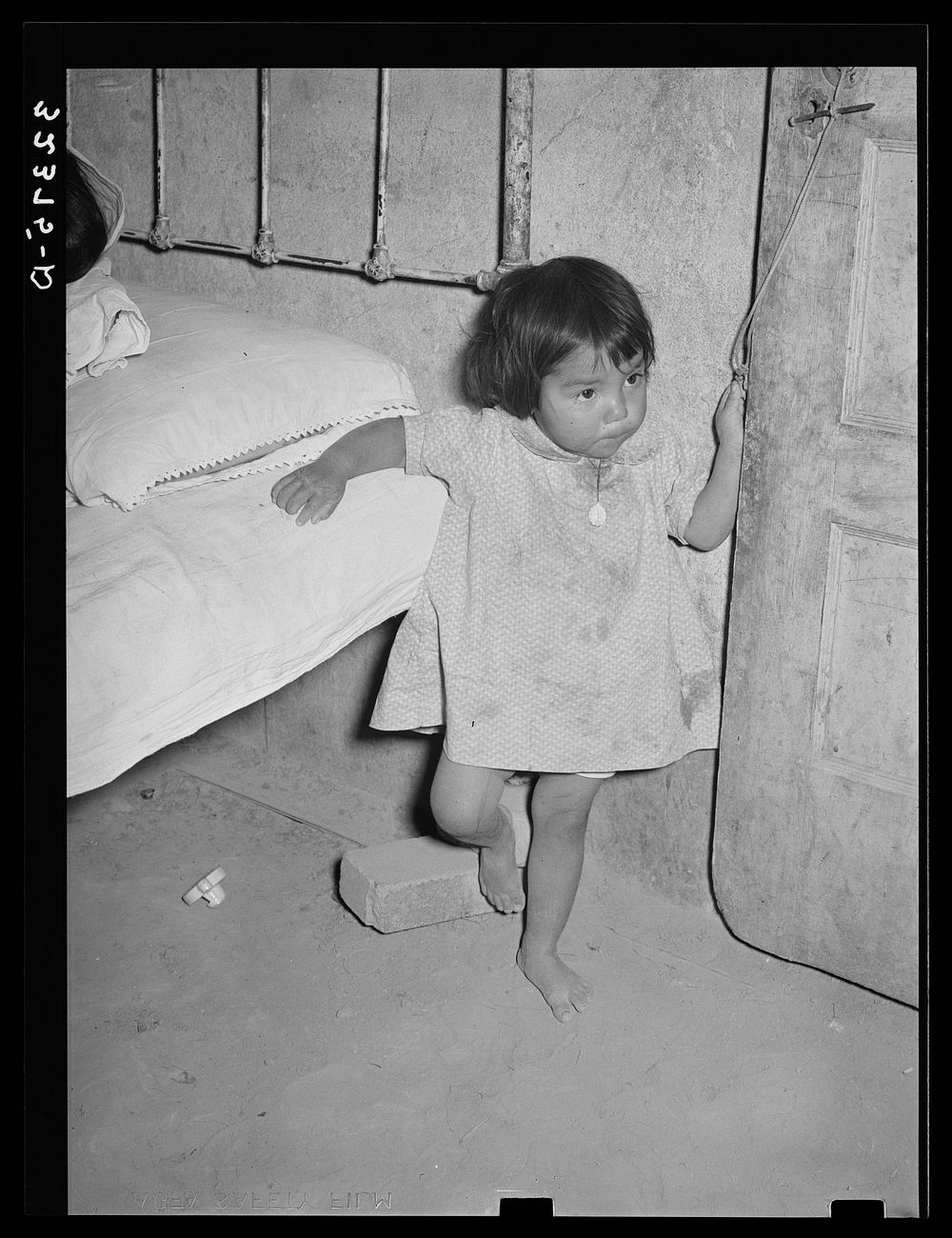 Mexican child in corner of room with dirt floor. Crystal City, Texas by Russell Lee