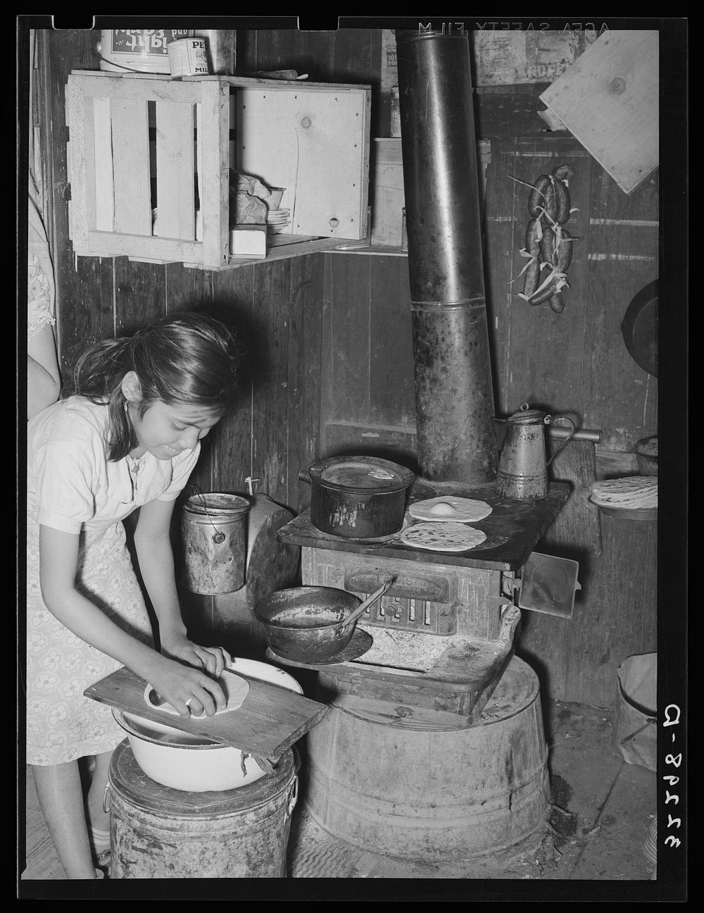 Mexican girl living in corral making tortillas. Tortillas can be seen baking on the stove. Robstown, Texas by Russell Lee
