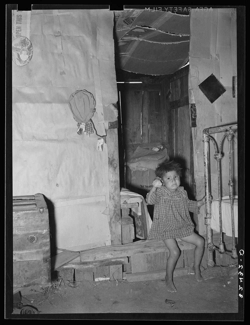 Mexican child sitting in doorway between living and bedroom in his home on the outskirts of San Antonio, Texas. Notice the…