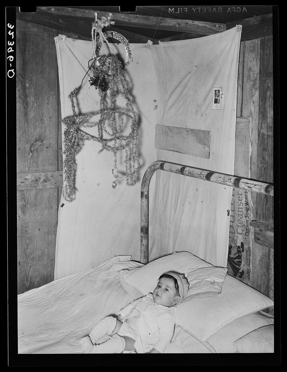 Mexican baby in bed with decorations above. Crystal City, Texas by Russell Lee