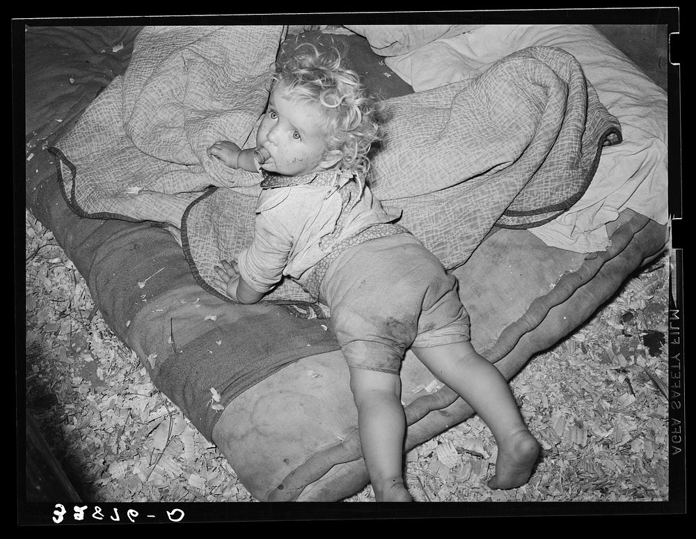 Child of  migrant strawberry picker on bed in tent near Hammond, Louisiana by Russell Lee