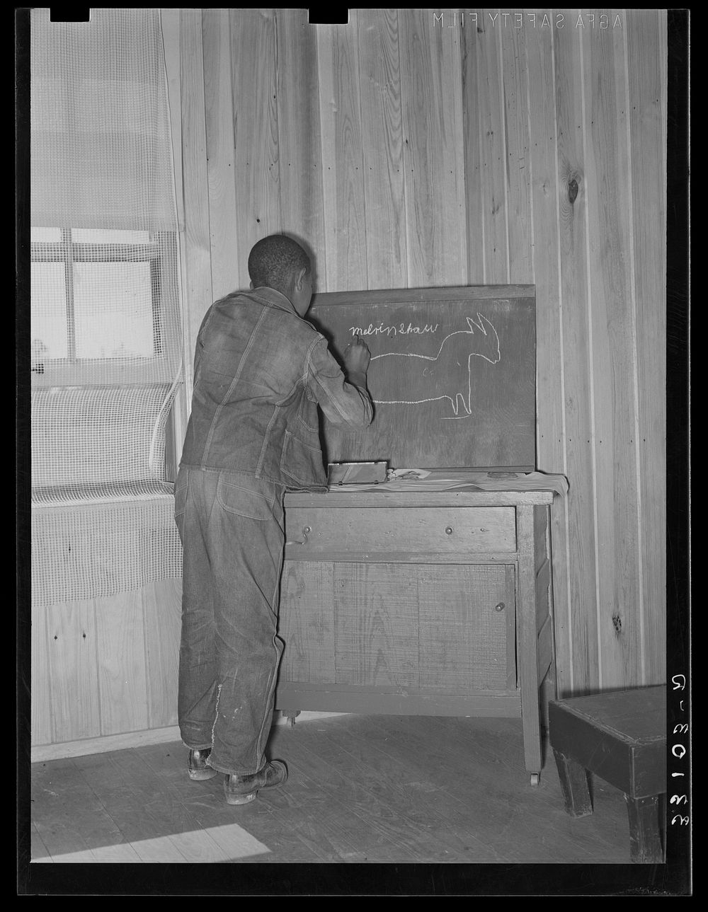 Son of FSA (Farm Security Administration) client writing name and drawing picture of mule on board in his home. Sabine…