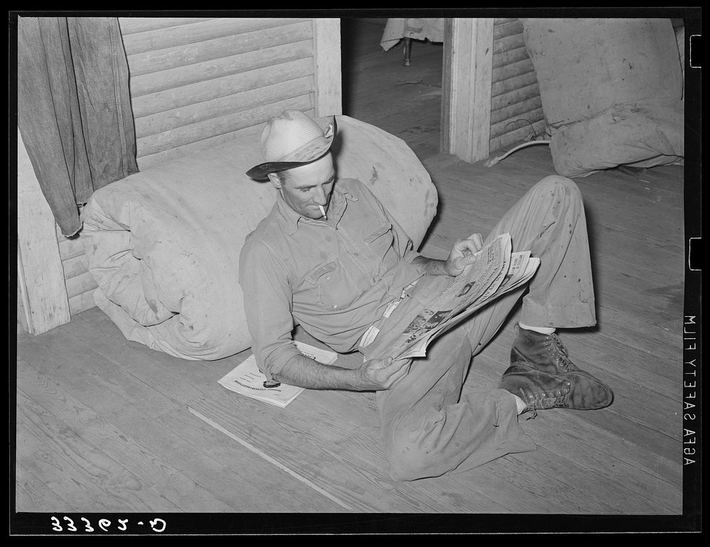 Cook of SMS Ranch propped against bedroll reading the paper. Bunkhouse on ranch near Spur, Texas by Russell Lee