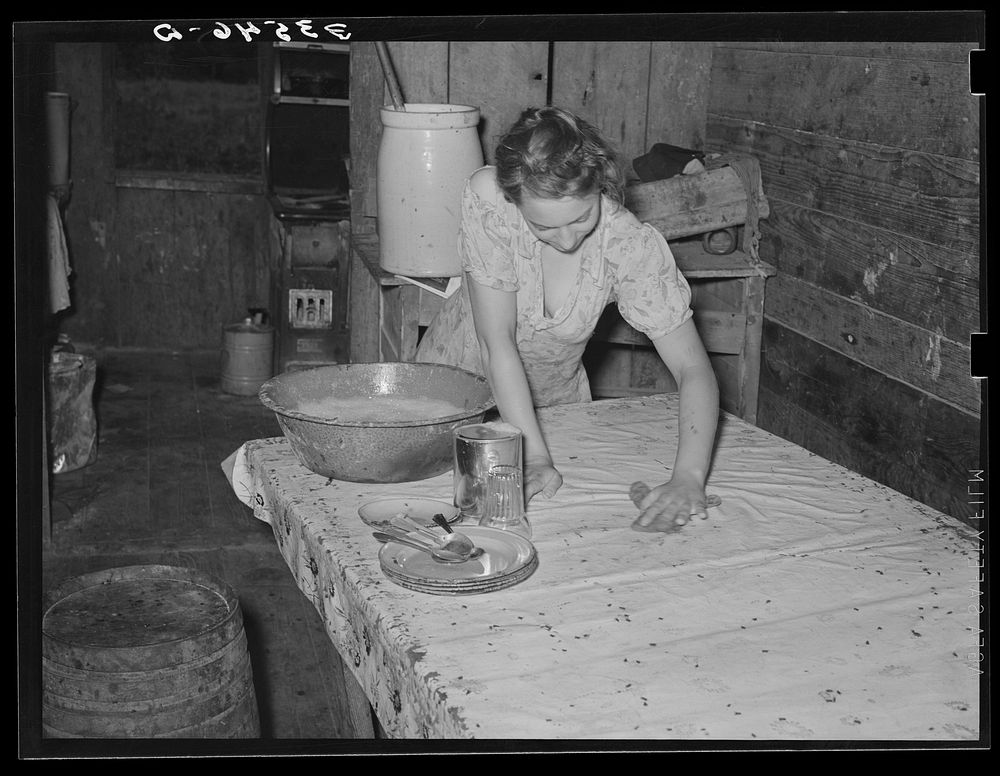 Daughter of agricultural day laborer cleaning up kitchen. Black spots on table cloth are flies. McIntosh County, Oklahoma by…
