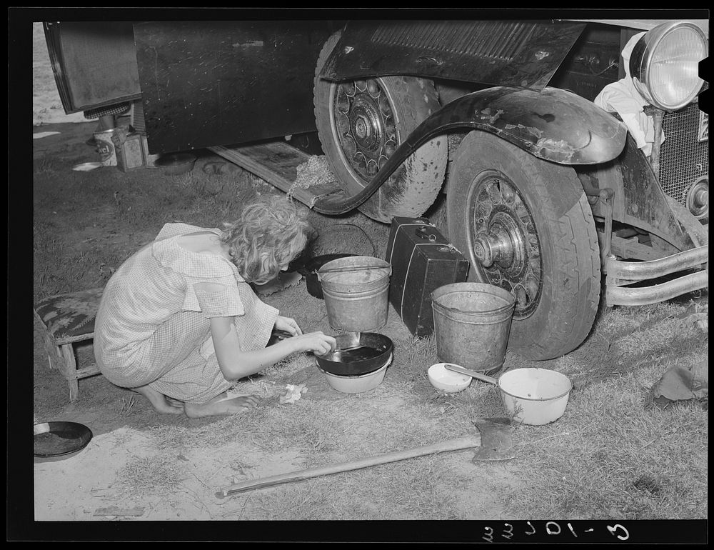Migrant girl gathering up pots and pans to pack into automobile at roadside camp near Muskogee, Oklahoma. Muskogee County by…