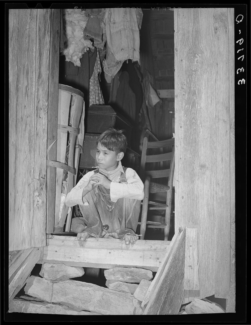 Indian child "hunkering down" in doorway of farm home near Sallisaw, Oklahoma. Hunkering down is an Indian slang term for…