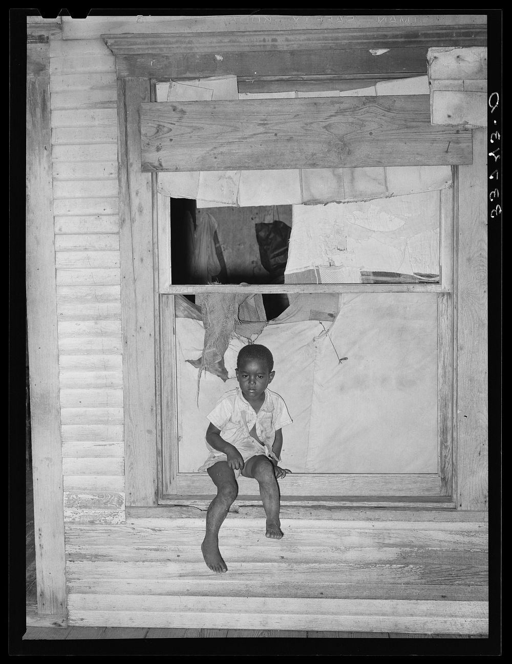 Son of  agricultural day laborer sitting in window of his home. Muskogee County, Oklahoma by Russell Lee