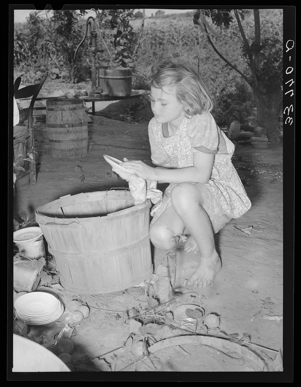 Daughter of migrant family wiping and packing dishes preparatory to leaving for California from Muskogee, Oklahoma by…