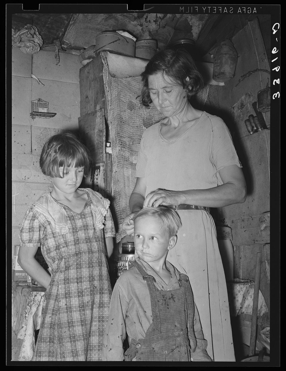 Woman in shack home in community camp. Oklahoma City, Oklahoma. Straightening her son's hair. Refer general caption no. 21…