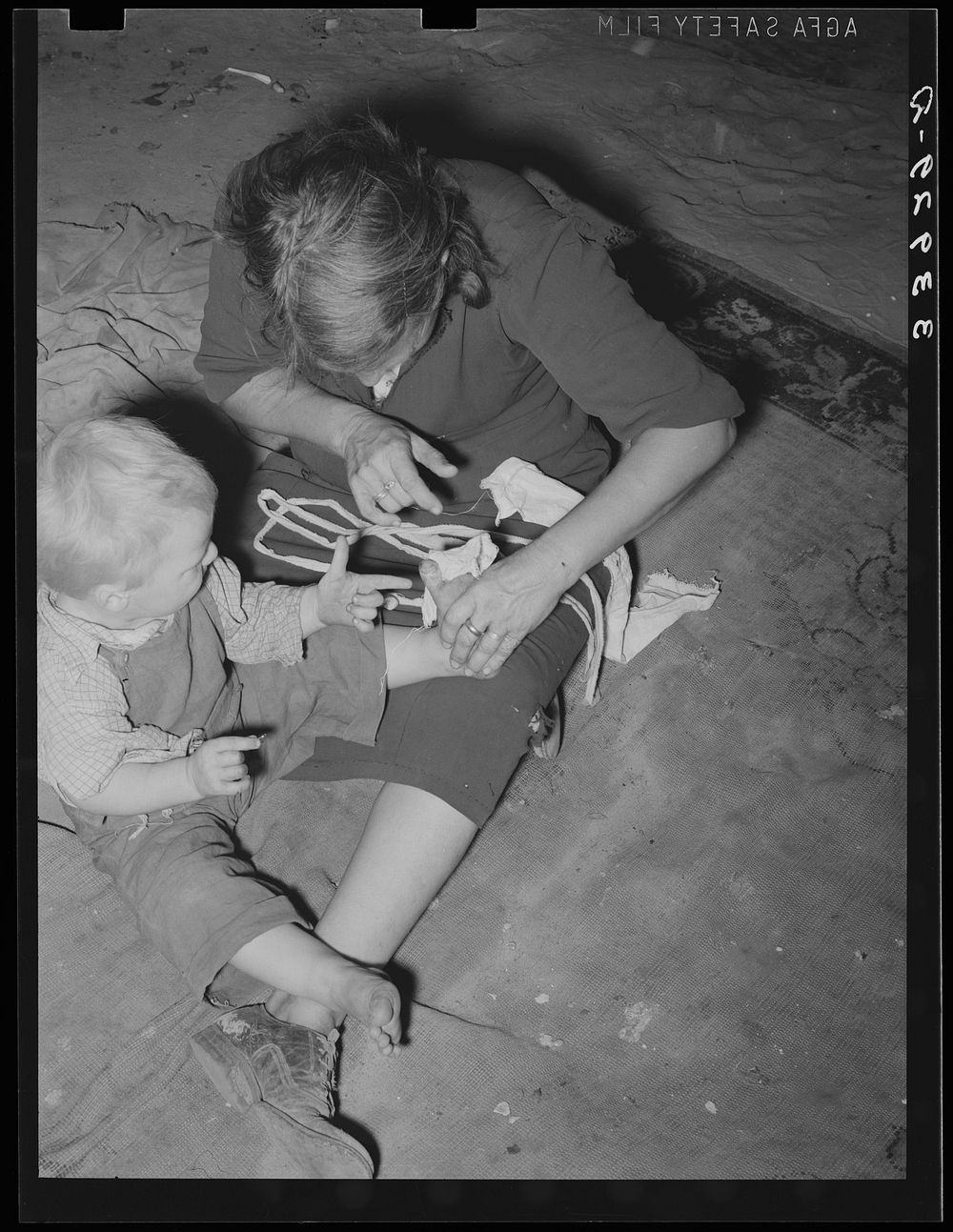 Mother bandaging toe of her son which was cut in debris of Mays Avenue camp. Oklahoma City, Oklahoma by Russell Lee