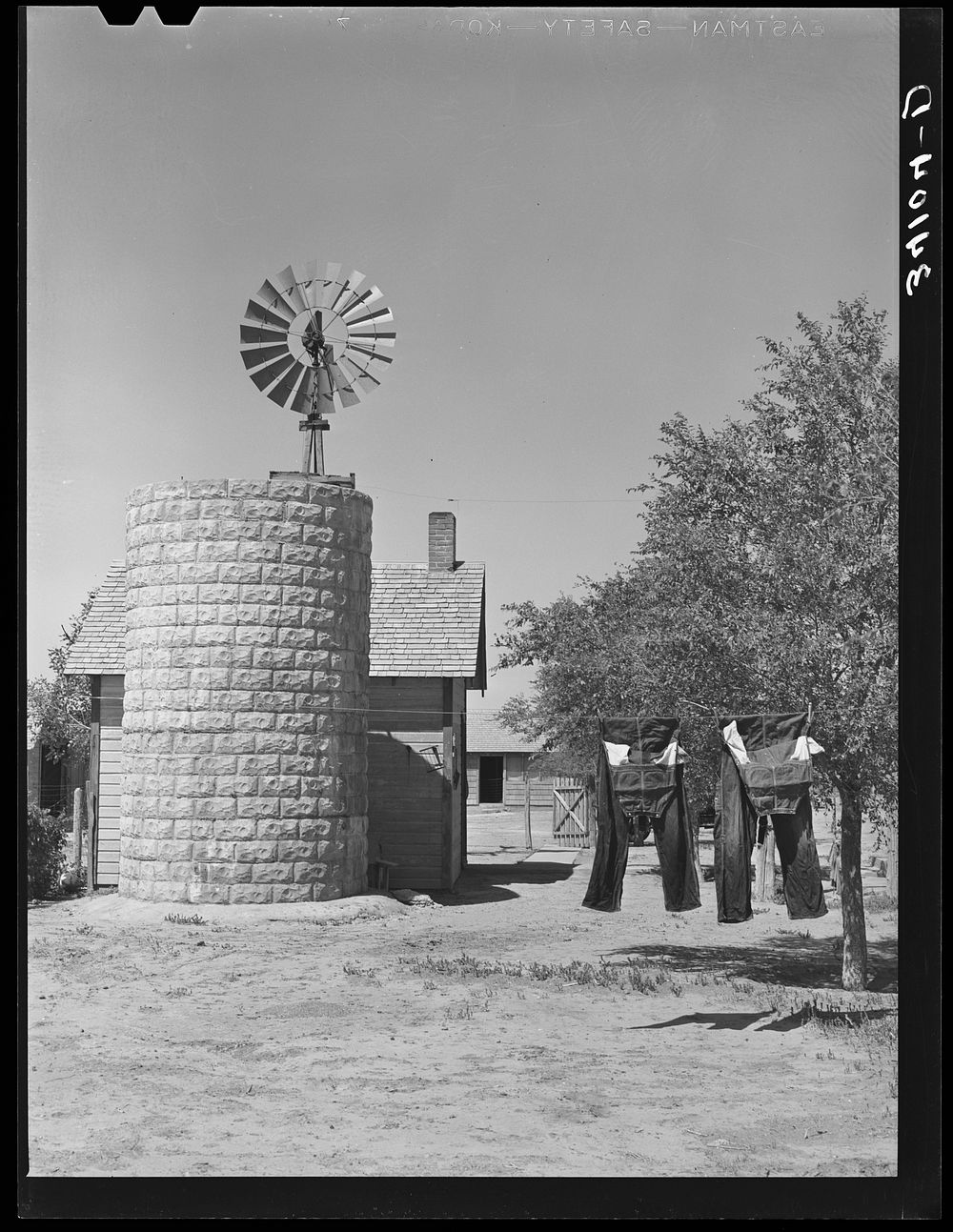 Silo, windmill and overalls on line on farmstead in Gray County, Kansas by Russell Lee