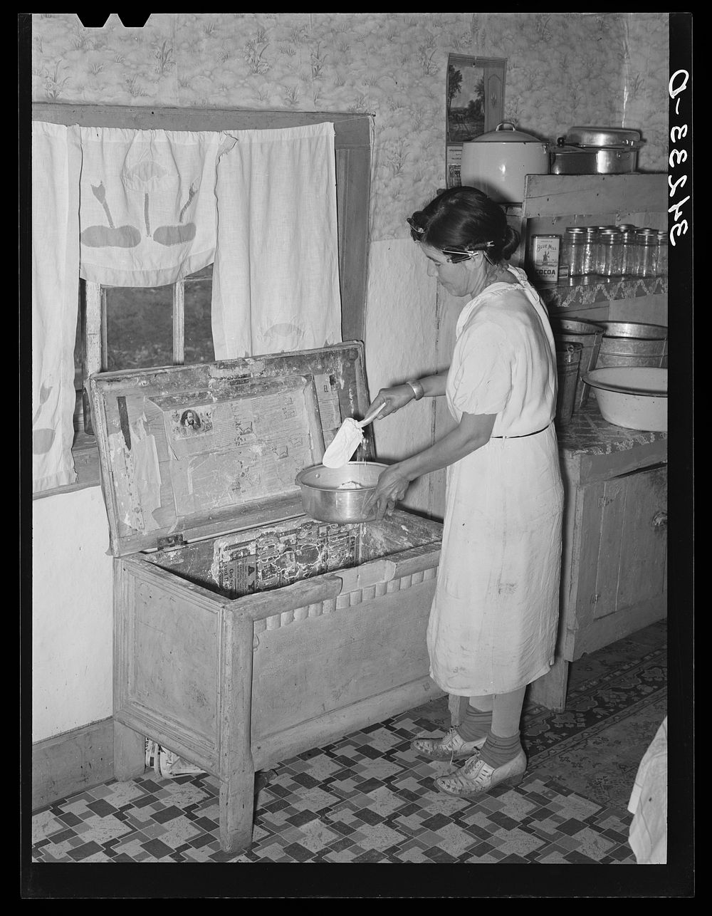 Spanish-American woman taking flour from old-type flour bin in her home near Taos, New Mexico by Russell Lee