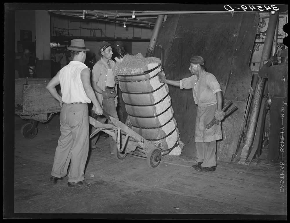 Guiding compressed bale of cotton onto hand truck. Compress, Houston, Texas by Russell Lee