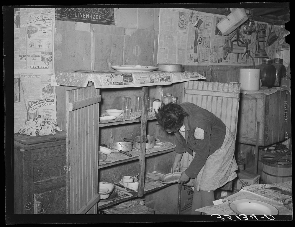 Removing plates from kitchen cupboard in home of Pomp Hall,  tenant farmer. Creek County, Oklahoma. See general caption…