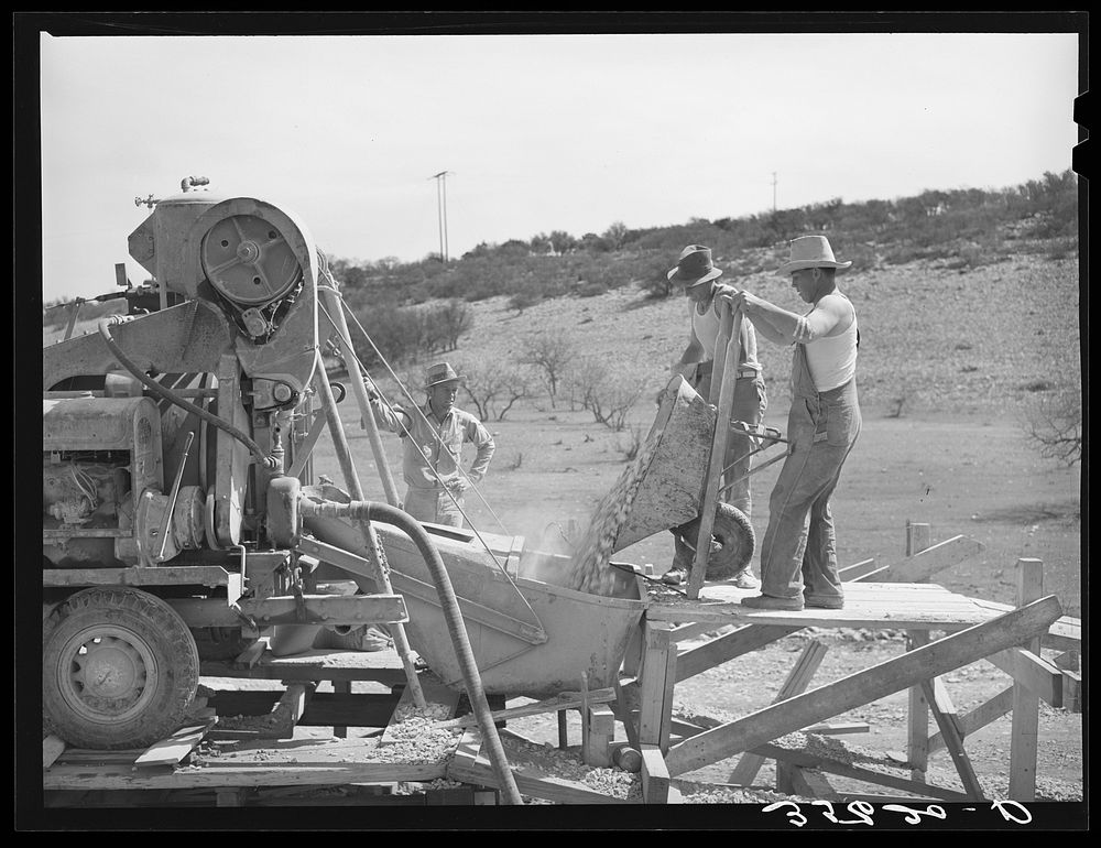 Road workers pouring gravel into concrete mixer. Menard County, Texas by Russell Lee
