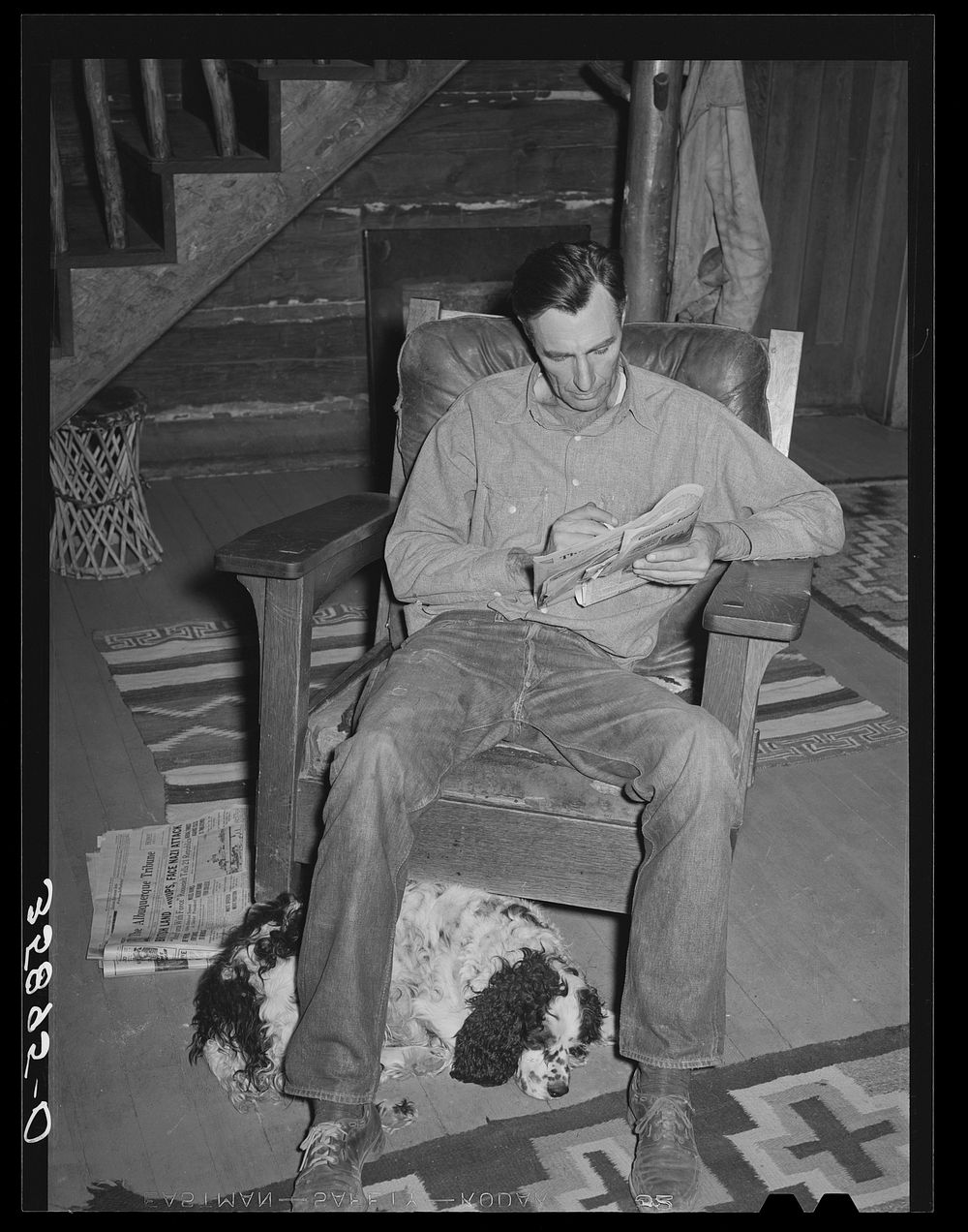 Manager of the Navajo Lodge working a crossword puzzle with his dog at his feet. Datil, New Mexico by Russell Lee