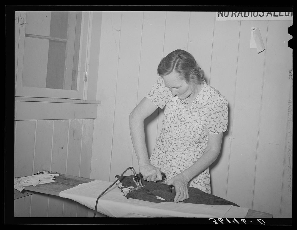 Wife of agricultural worker ironing at the Agua Fria migratory labor camp. Arizona by Russell Lee