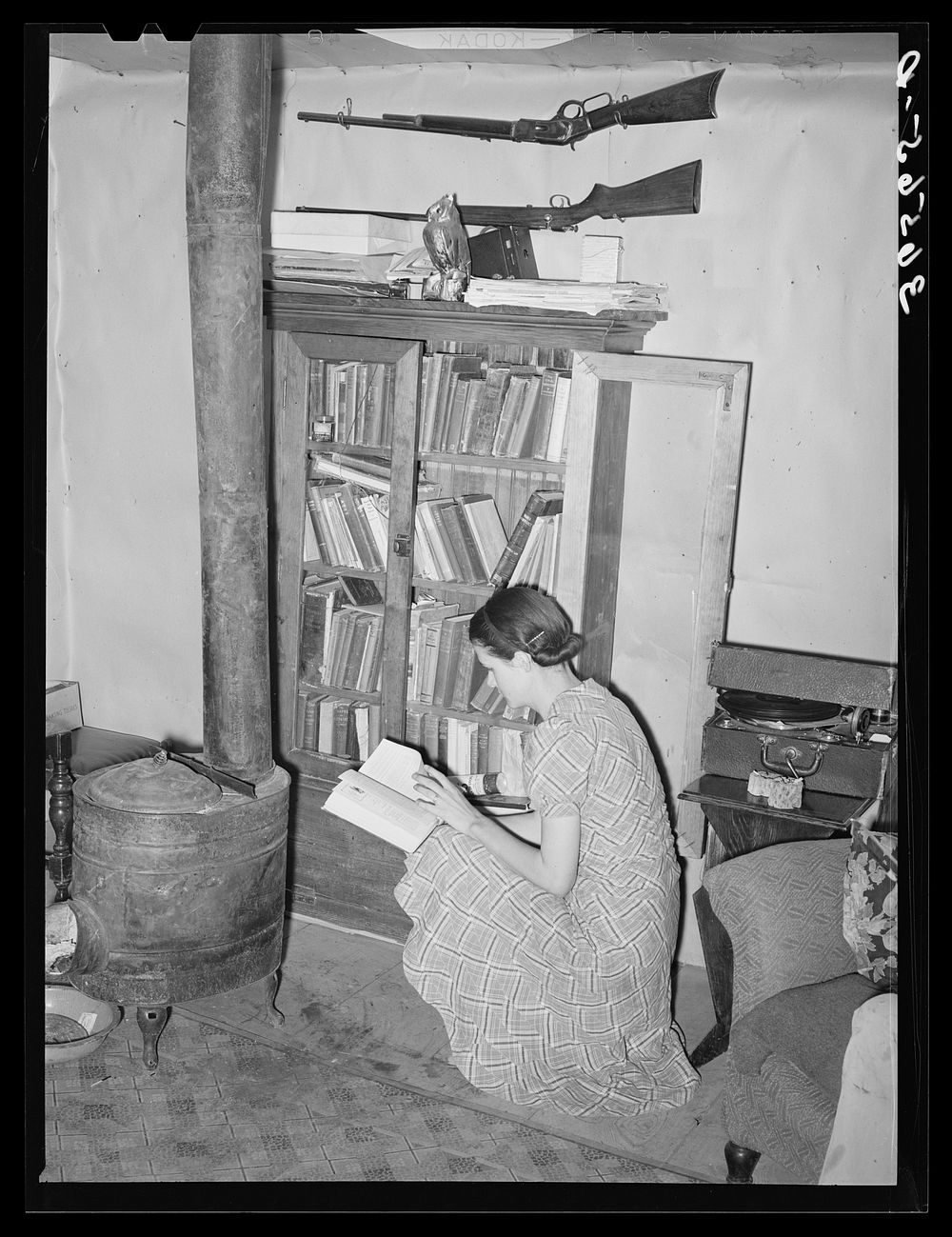 Wife of farmer at her bookcase in her log home. Pie Town, New Mexico by Russell Lee