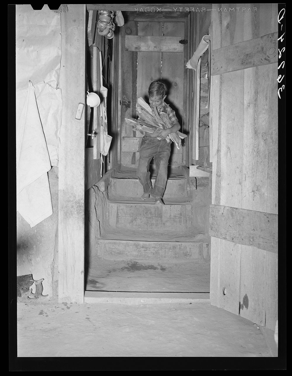 Jack Whinery's young son coming down the steps into the dugout with an armload of wood. Pie Town, New Mexico by Russell Lee