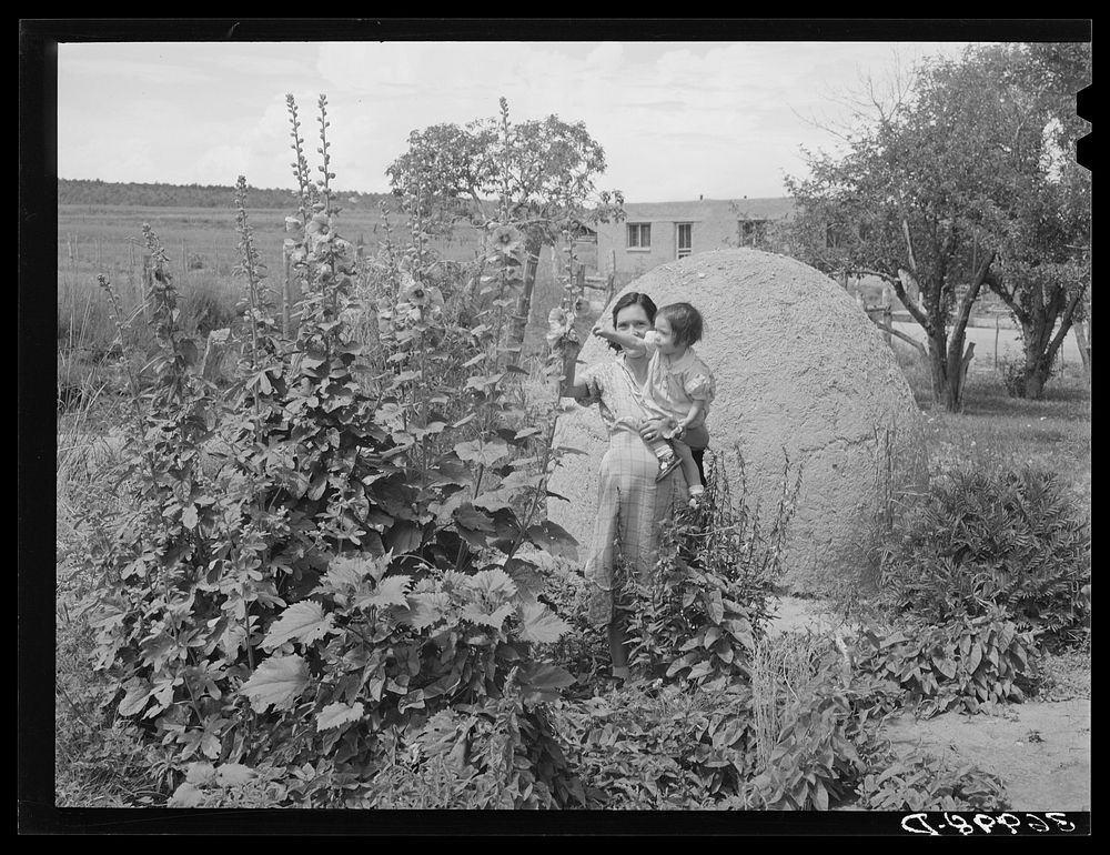 Spanish-American woman and baby in flower garden. Chamisal, New Mexico by Russell Lee