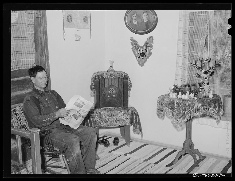 Spanish-American farmer reading in living room of his home. Chamisal, New Mexico by Russell Lee