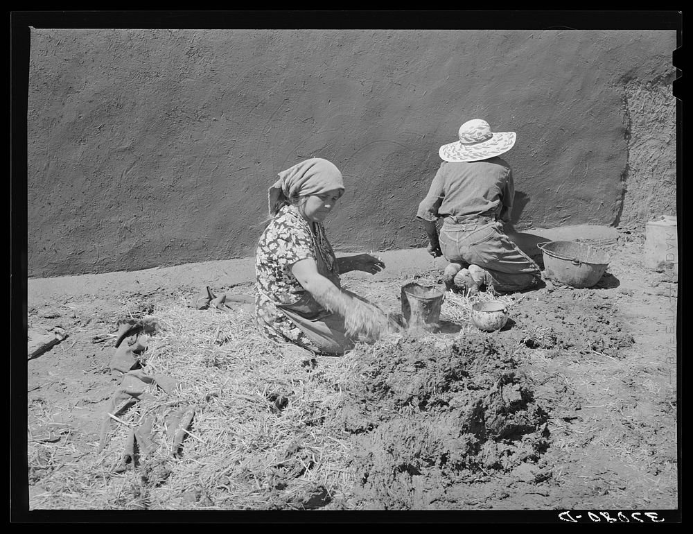 Spanish-American women making plaster of straw and mud to replaster house. Chamisal, New Mexico by Russell Lee