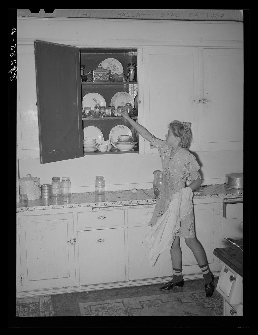Daughter of Morman [i.e. Mormon] farmer putting away dishes in kitchen cabinet. Box Elder County, Utah by Russell Lee