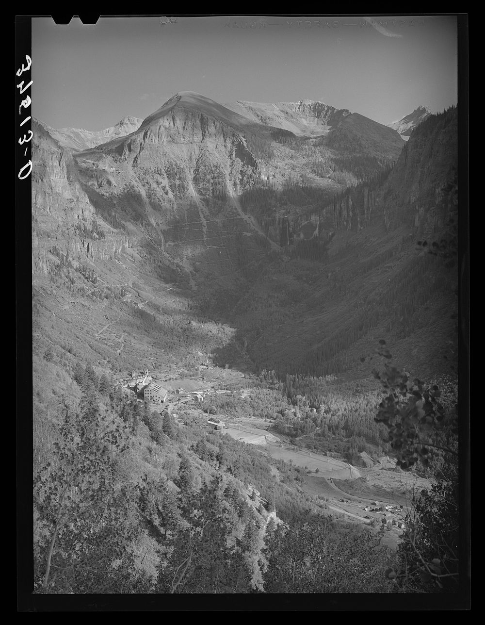 Mountain valley near Telluride showing gold mill and Bridal Veil Falls and road winding around mountain up to the mine. San…