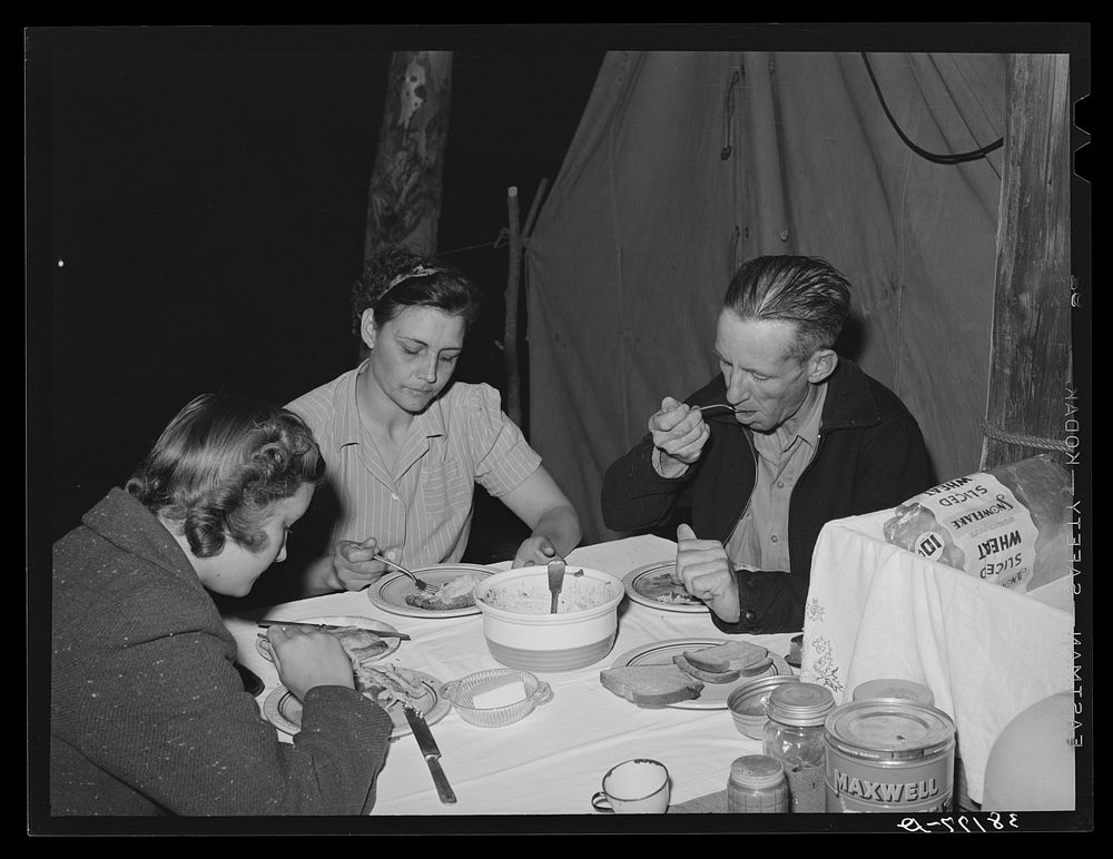 Carpenter, his wife and daughter eating supper in front of their tent-home. Mission Valley, California, about three miles…