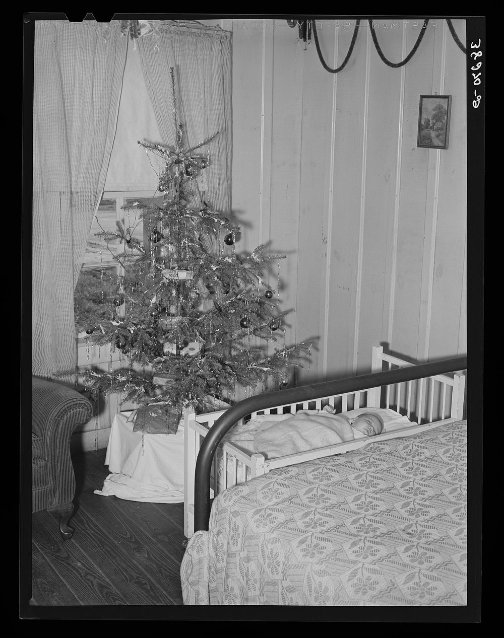 Baby and Christmas tree in corner of living room in home of construction workman. This family came to Corpus Christi from…