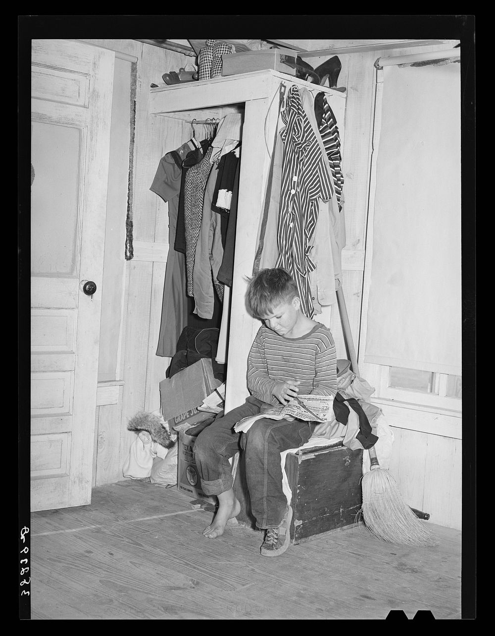 Small boy, son of carpenter from Hobbs, New Mexico, reading funny papers in corner of room in tourist court. Lack of…