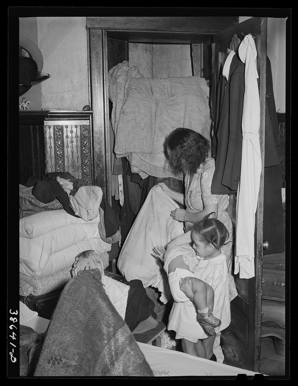 Corner of bedroom with  housewife examining bed clothing chewed by rats. Chicago, Illinois by Russell Lee