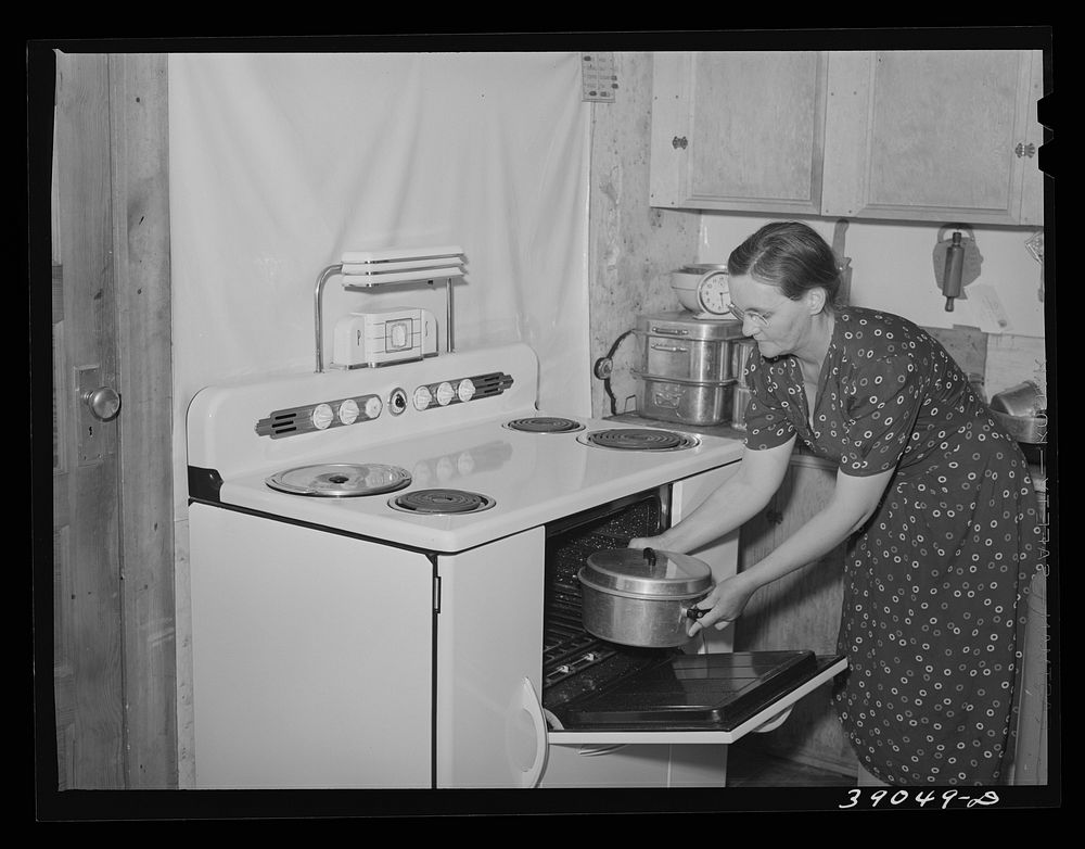 Wife of Mr. E.E. Botner, FSA (Farm Security Administration) rehabilitation borrower, putting roasting pan into electric…