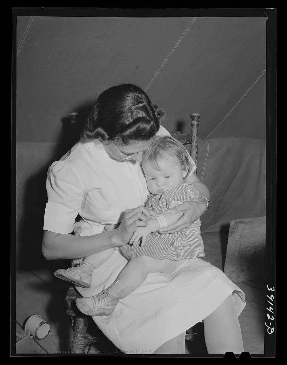 Nurse looks at cut on baby's arm at the FSA (Farm Security Administration) migratory labor camp mobile unit. Wilder, Idaho.…